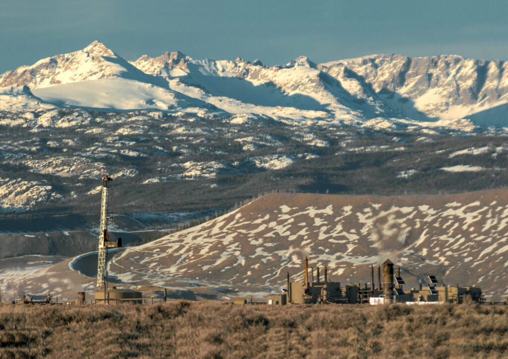 Rugged mountain peaks covered by snow with natural gas injection well and storage facility in the foreground.